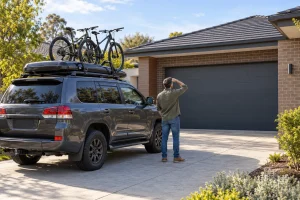 A loaded 4WD parked clear of a closed garage door while an owner checks roof-rack clearance.